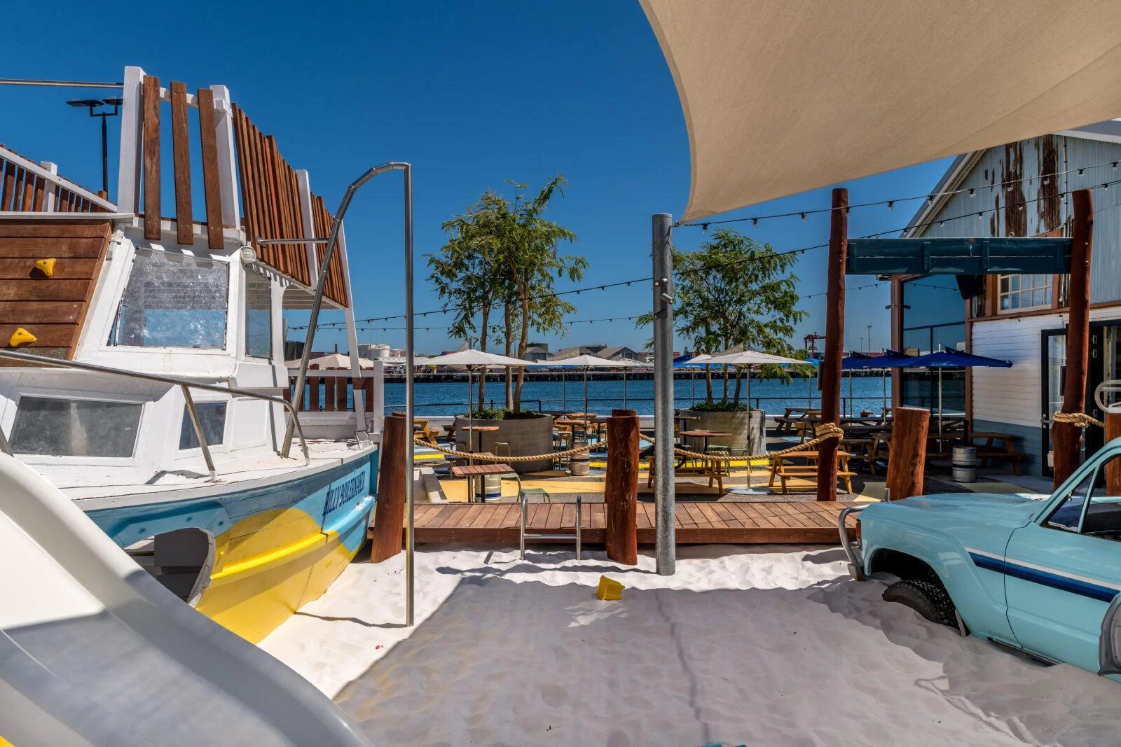 Coastal playground courtyard at Gage Roads Brewery Fremantle showing custom crayfishing boat play structure, repurposed car, and waterfront dining deck