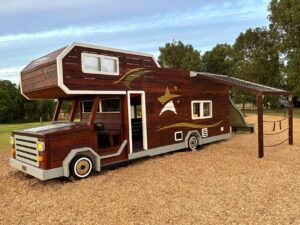 524-MTH Motorhome — front three-quarter view at dusk alongside companion spider web net climber and disc swing equipment, holiday park Dunsborough WA