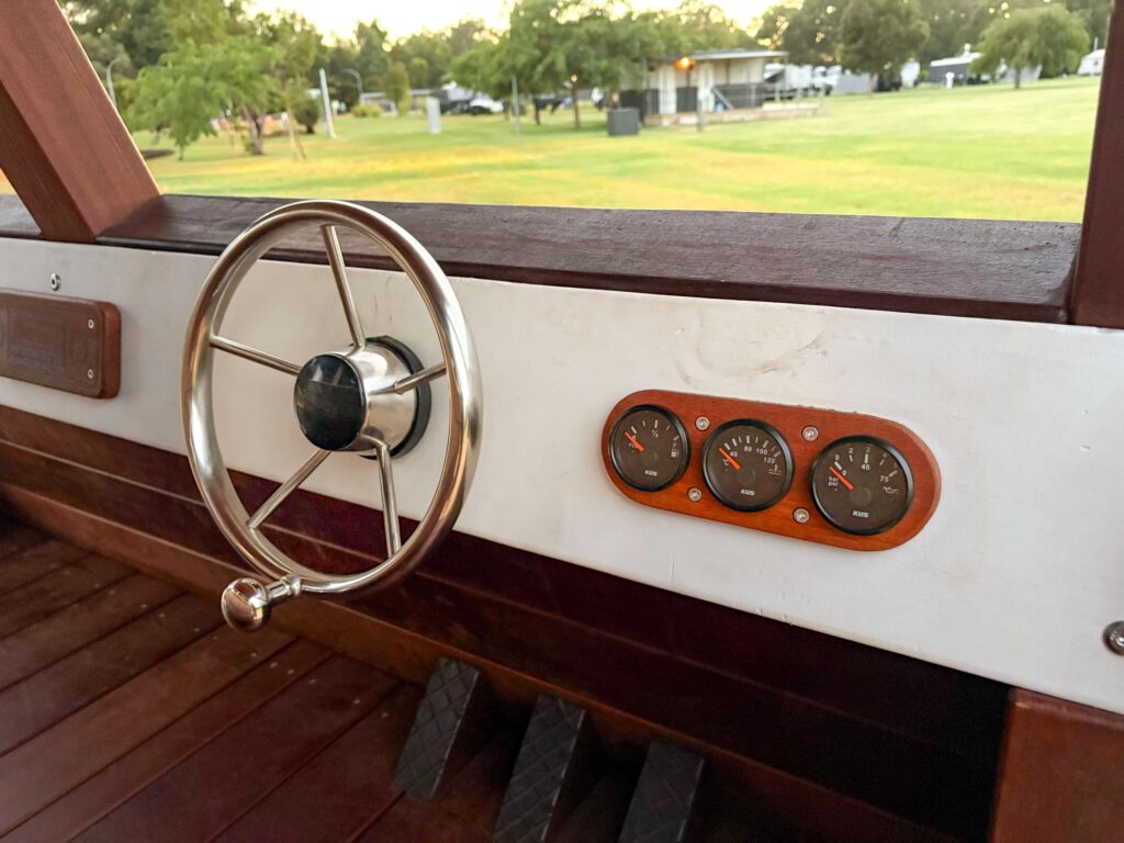 524-MTH Motorhome — stainless steel steering wheel and Jarrah-mounted instrument gauges inside driver's cabin, looking out to park