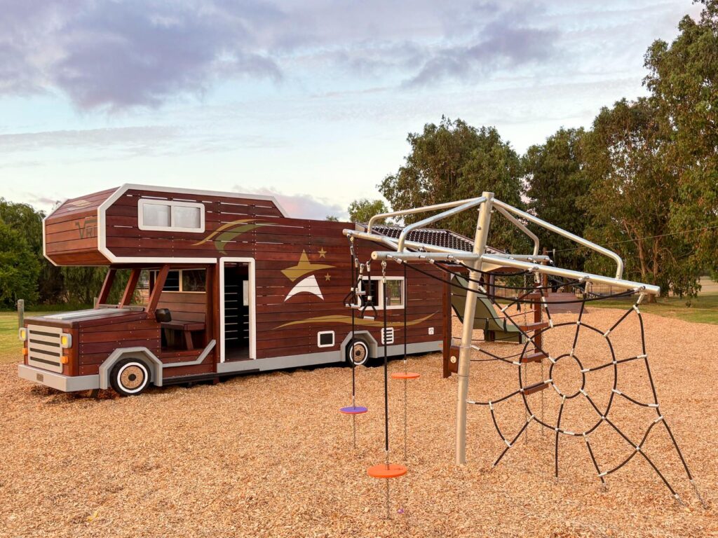 524-MTH Motorhome — full passenger-side profile showing mud-splash climbing wall, double slide and swinging hammock at dusk