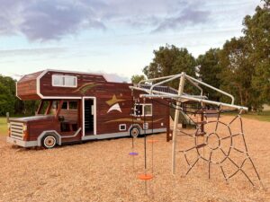 524-MTH Motorhome — full passenger-side profile showing mud-splash climbing wall, double slide and swinging hammock at dusk