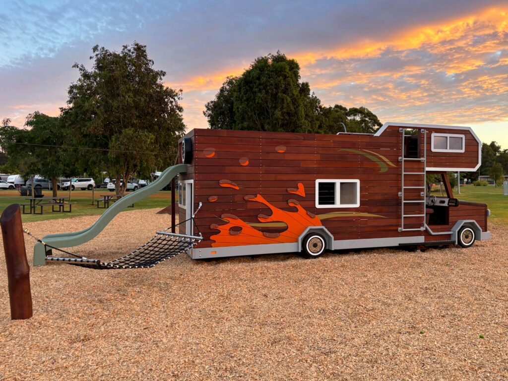 524-MTH Motorhome — rear passenger side at orange sunset showing mud-splash climbing wall holds, hammock and upper deck ladder