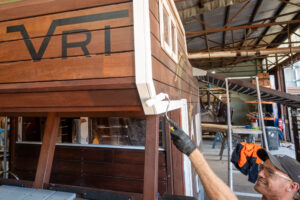 VRI craftsman painting the 524-MTH Motorhome window trim in the O'Connor WA workshop — handcrafted Jarrah playground equipment