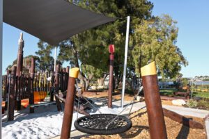 Mini Double Pole Basket Swing at Shelley Beach Park playground, Pelican Nest Fort and shade sail in background, Canning River foreshore