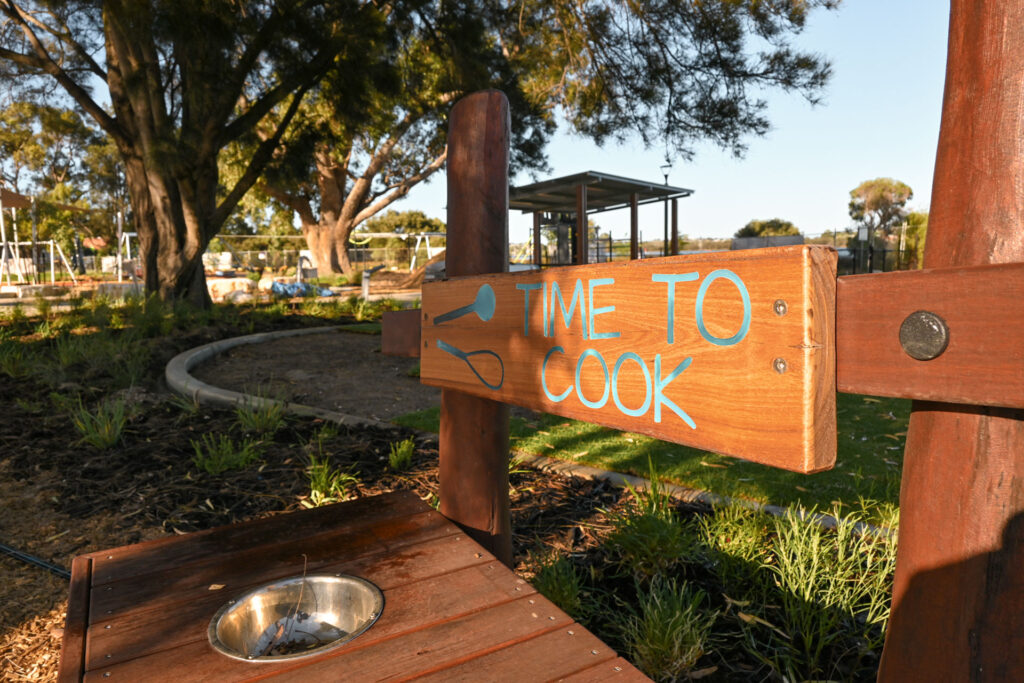 Time to Cook painted sign on the Little Cooker Kitchen play structure at Shelley Beach Park playground, Jarrah timber, native vegetation in background
