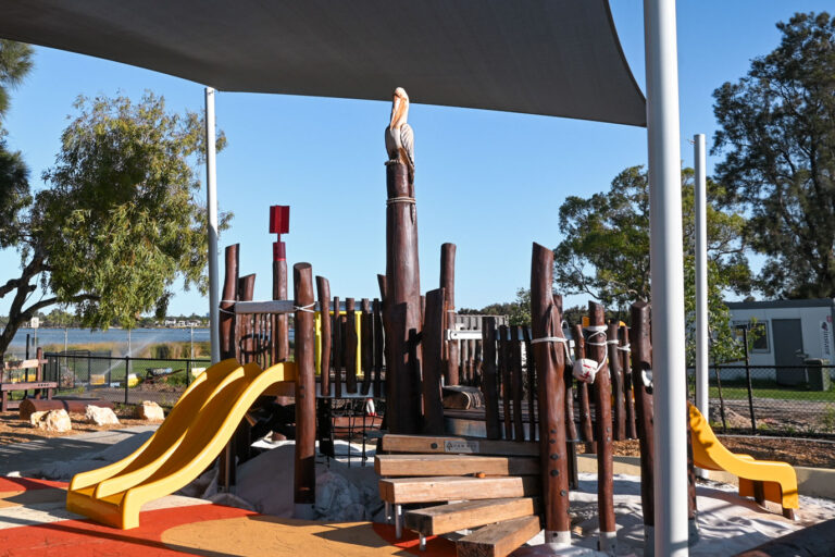Shelley Beach Park playground overview — custom timber play structure, shade sail and Aboriginal-design rubber surfacing on the Canning River foreshore