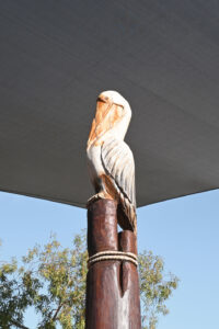 Hand-carved painted pelican sculpture at the summit of the Pelican Nest Fort, Shelley Beach Park playground — Jarrah bush pole, shade sail and blue sky