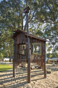Jarrah timber cubby shack with vertical board cladding and elevated platform at Hathaway Reserve playground Baldivis