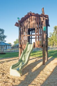 Rear view of Jarrah timber cubby shack with elevated platform slide and pitched roof at Hathaway Reserve playground Baldivis