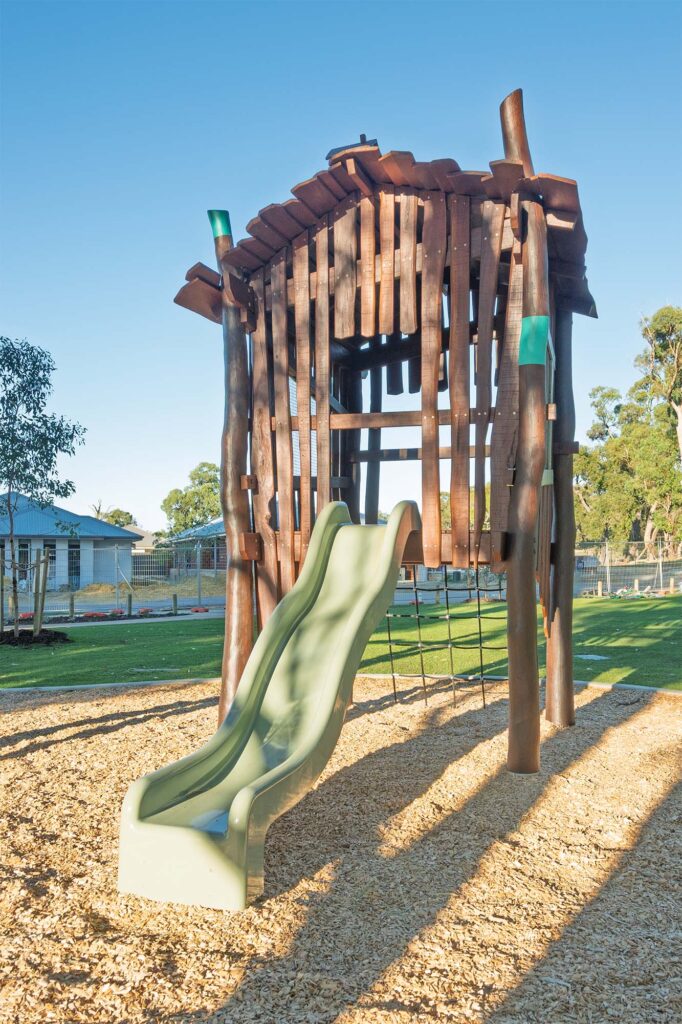 Rear view of Jarrah timber cubby shack with elevated platform slide and pitched roof at Hathaway Reserve playground Baldivis