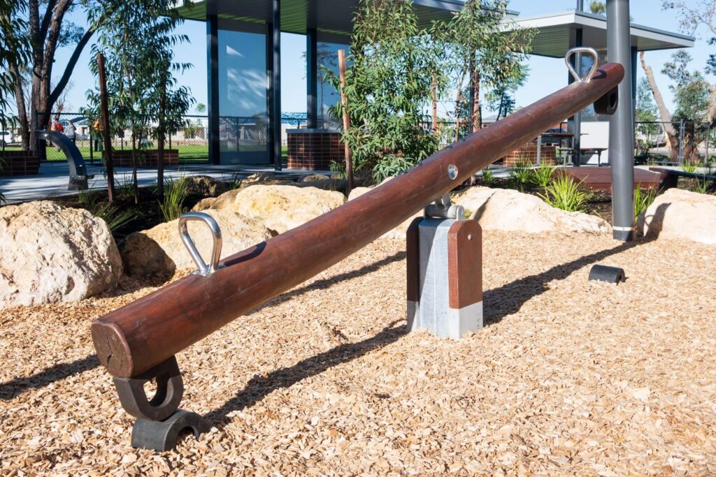 Jarrah timber see saw with stainless steel handles and rocking mechanism among landscaping rocks at Baldivis Parks Stage 17 playground