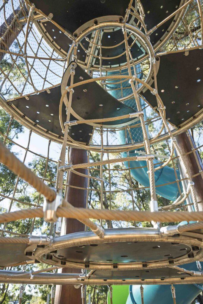 Wide angle interior of Jarrah climbing tower showing circular stainless steel rings rope tunnels and teal tube slide at Hathaway Reserve playground Baldivis