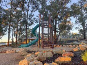 Jarrah timber climbing tower playground with teal tube slide set among mature trees and rock landscaping at Hathaway Reserve Baldivis